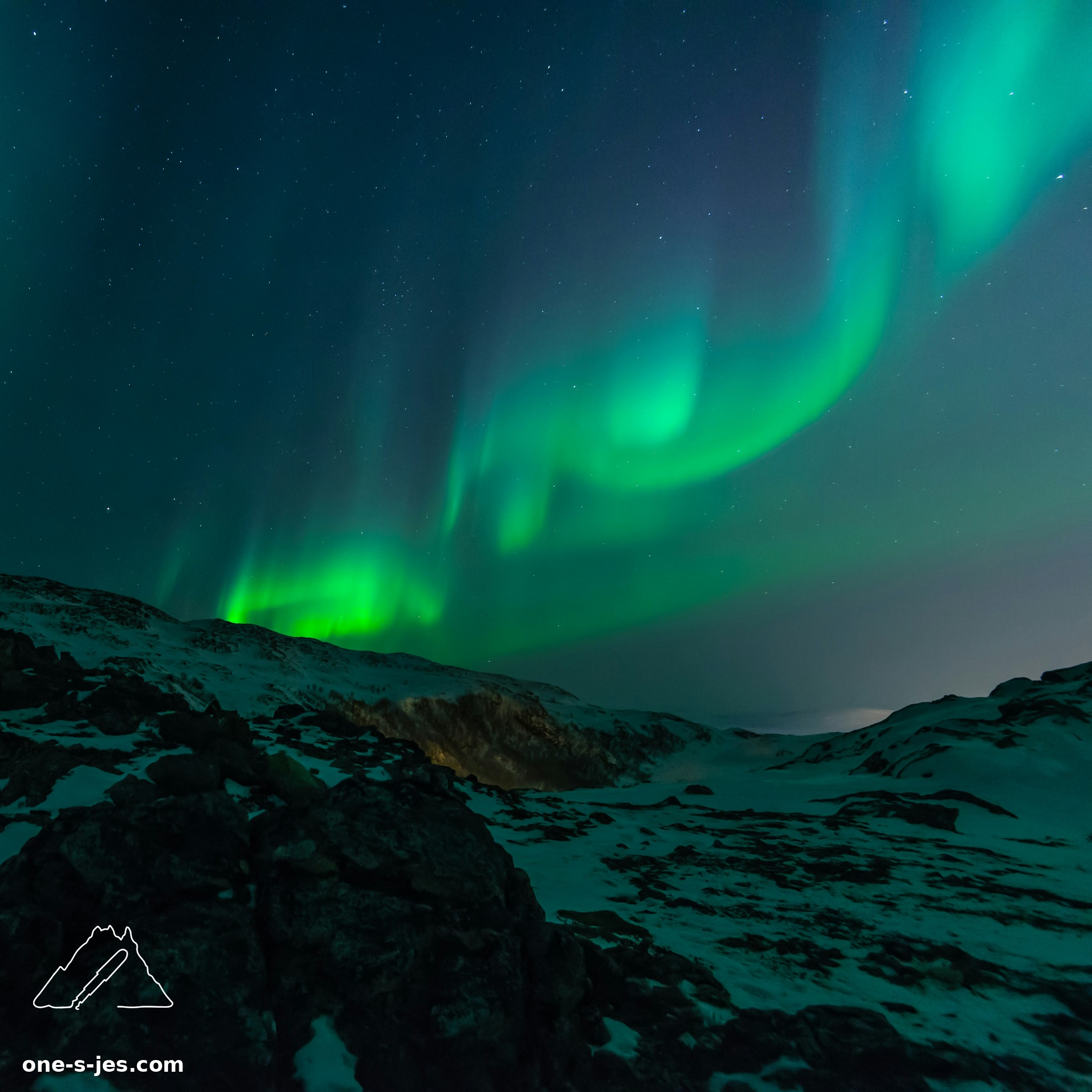 Northern lights over a snowy landscape at night with One S Jes logo and website text in the bottom left